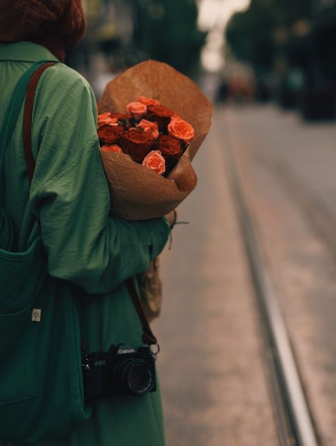 Person holding a bouquet of red roses and DSLR camera on a city street, creating a warm and artistic urban vibe.