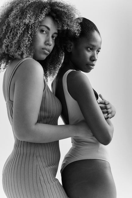 Fashionable black and white portrait of two stylish women embracing in a studio setting.