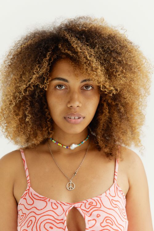 Free Close-up portrait of a woman with curly hair and colorful necklace in a tank top, looking at camera. Stock Photo