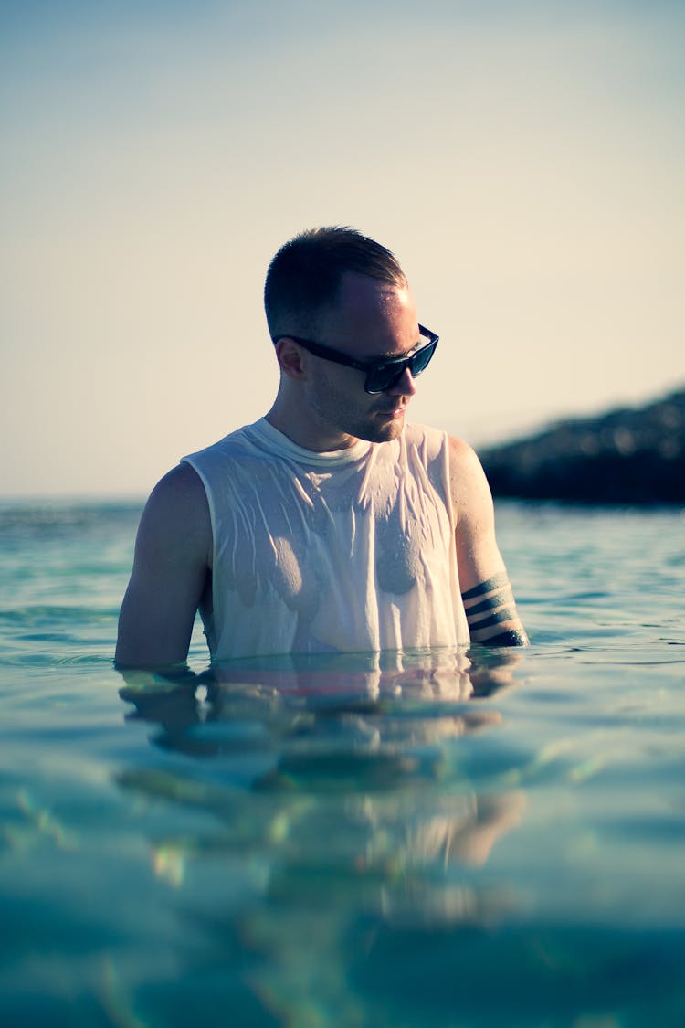 Man In White Tank Top Wearing Black Sunglasses Standing In Water