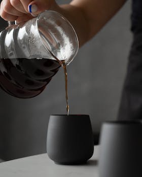 Close-up of coffee being poured into a sleek black cup in a minimalist setting.