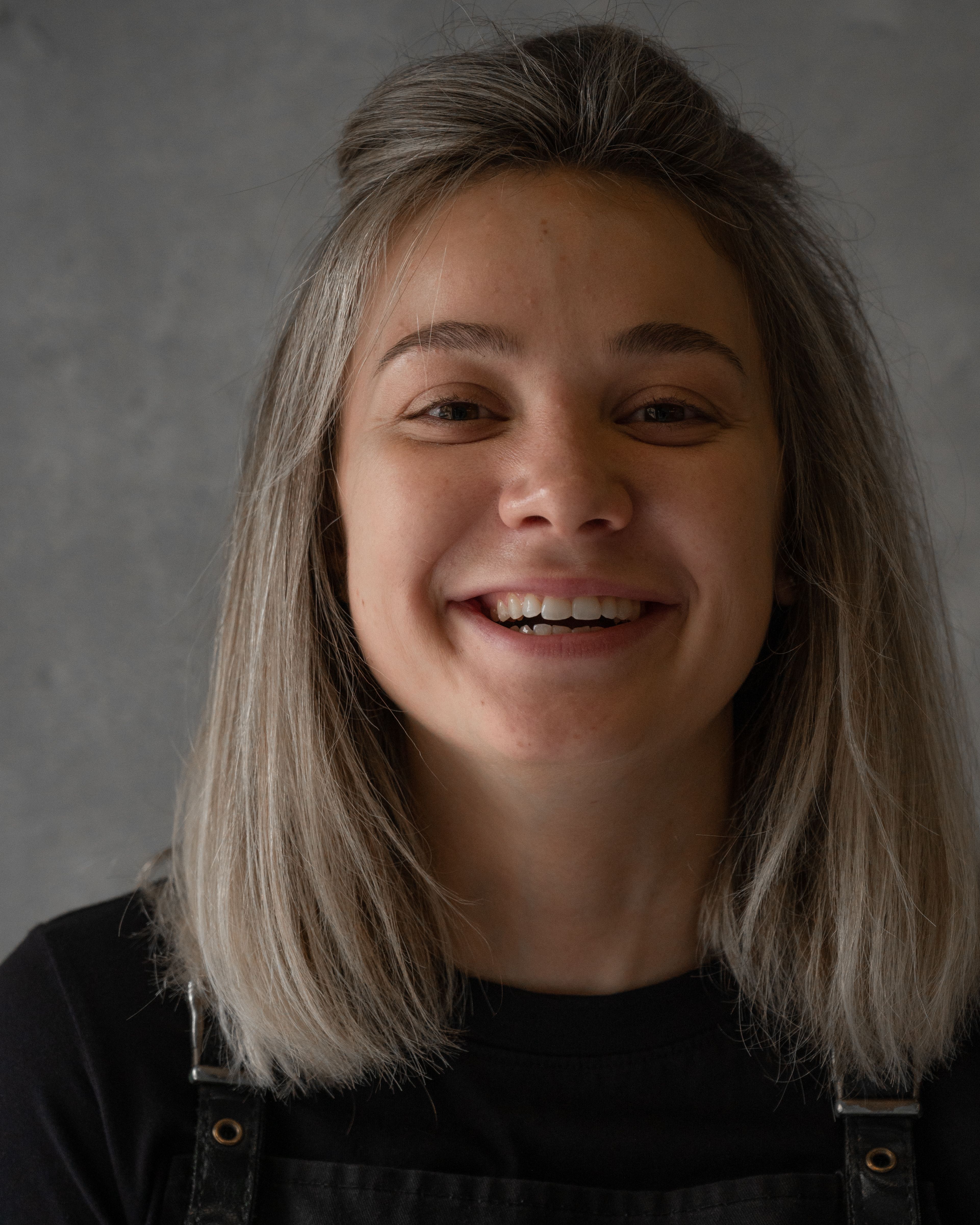Candid portrait of a smiling woman with blonde hair against a gray background.