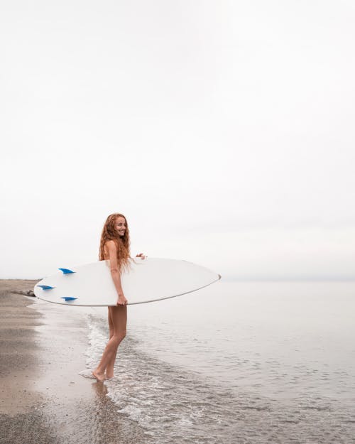 一個女人站在海灘上拿著她的衝浪板