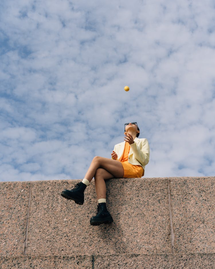 Woman Sitting On Wall And Throwing Fruit