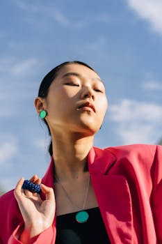 Stylish portrait of a woman in a pink blazer with chic accessories, set against a clear sky.