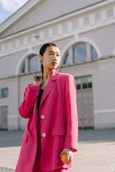 A fashionable young woman poses outdoors in a vibrant pink blazer.