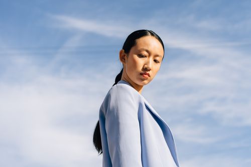 Free Fashionable woman gazing down, wearing a blue jacket against a clear sky. Stock Photo