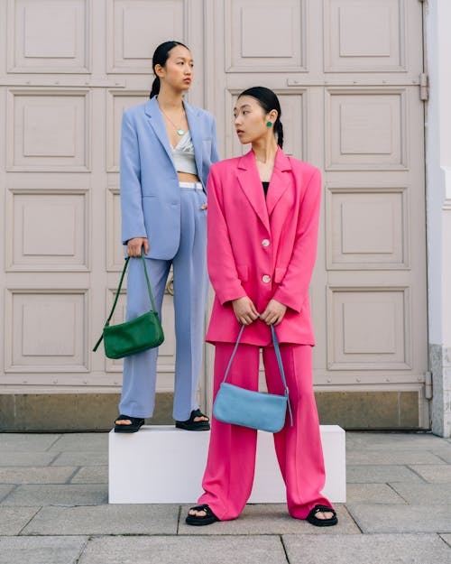 Women in Pink and Blue Blazers Standing on the Street while Holding Bags