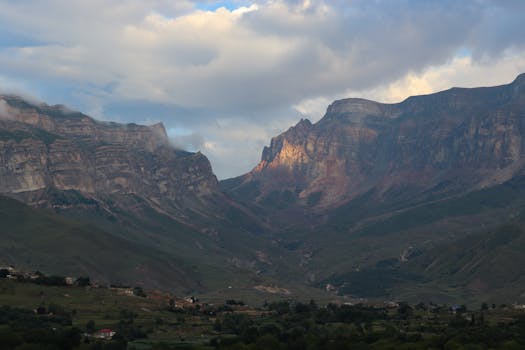 Dramatic mountain landscape with clouds casting shadows over a vibrant valley.