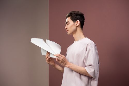 Free Profile of a young man posing with a paper plane in a studio setting. Stock Photo