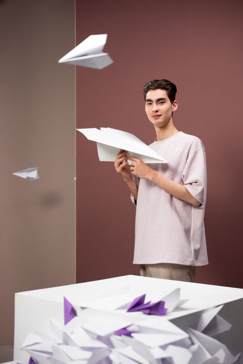 Free Young man in a white shirt standing with paper airplanes against a maroon background. Stock Photo