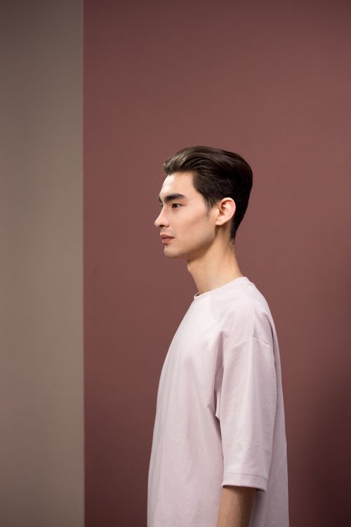 Free Side profile of a young man in a white shirt against a maroon background, showcasing a modern hairstyle. Stock Photo