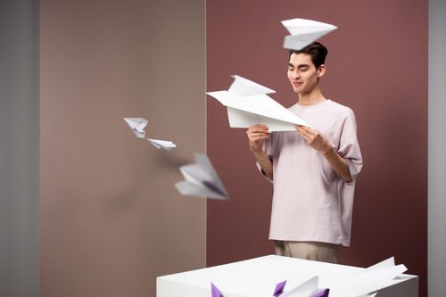 Free A young man enjoying paper airplanes in a unique studio setting, capturing a playful moment. Stock Photo