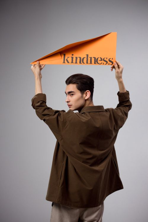 Free Asian man holding a 'Kindness' sign overhead in a studio setting, expressing positivity. Stock Photo