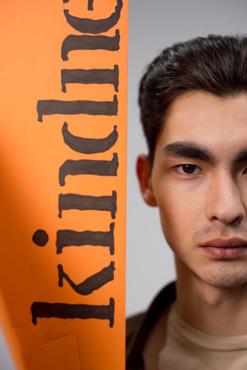 Free Half-face portrait of a man with 'Kindness' sign on orange paper, emphasizing kindness theme. Stock Photo