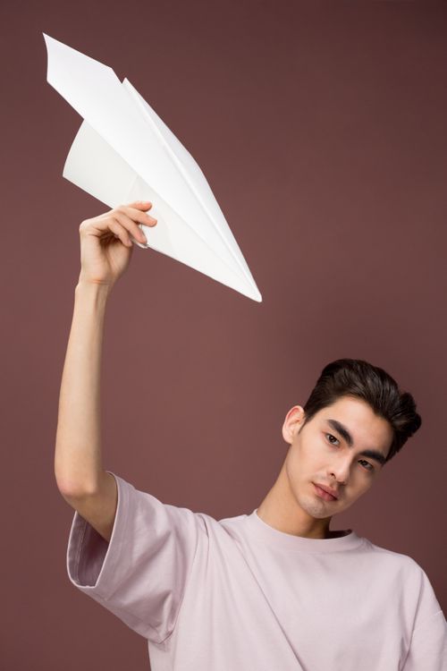 Free Portrait of a young man with a paper airplane against a simple background, looking at the camera. Stock Photo
