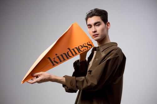 Free Stylish man holding an orange paper airplane with 'kindness' text on a white background. Stock Photo