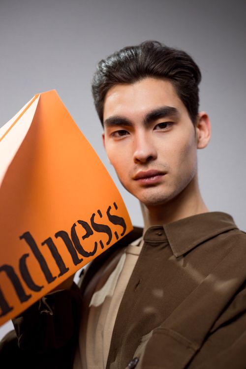 Free Young man with short hair poses with an orange sheet featuring word 'kindness'. Stock Photo