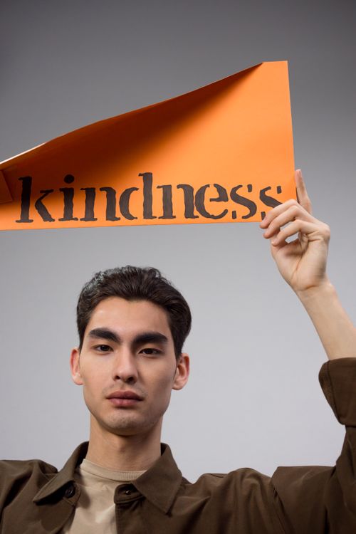 Free Man holds orange paper sign with 'kindness' text, promoting positive message. Stock Photo