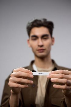 A young man in a blurred background holding a paper with 'Charity' text. — photo by Ron Lach