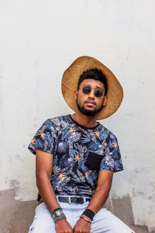 Free Fashionable man in floral shirt and straw hat posing against a textured white wall. Stock Photo