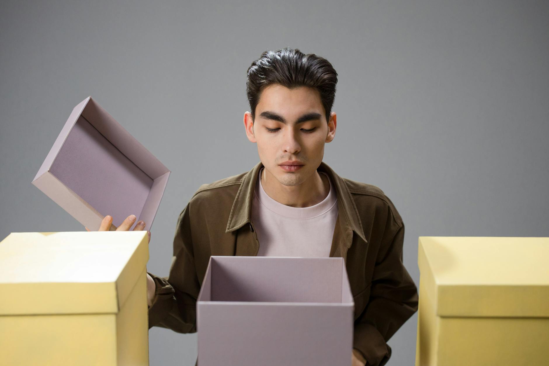 Man opening and examining a box on a neutral background, expressing curiosity and contemplation.