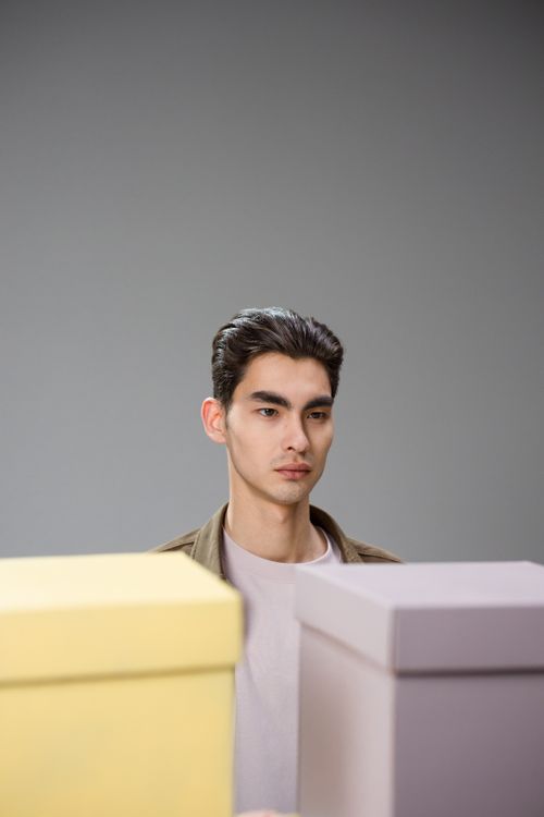 Free Serious man posing behind pastel colored boxes in a minimalistic studio setting. Stock Photo