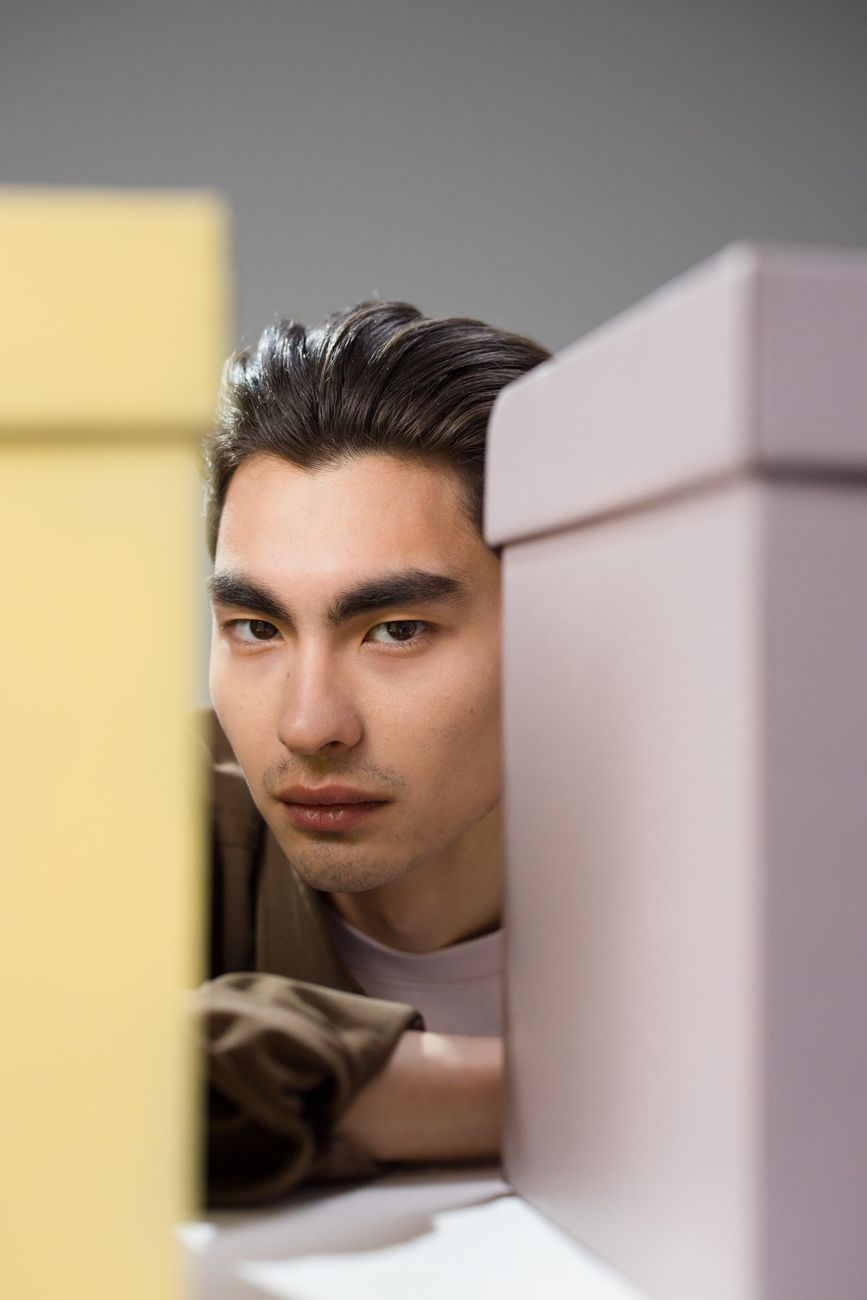 A man with a serious expression is surrounded by pastel-colored gift boxes in a studio setting.