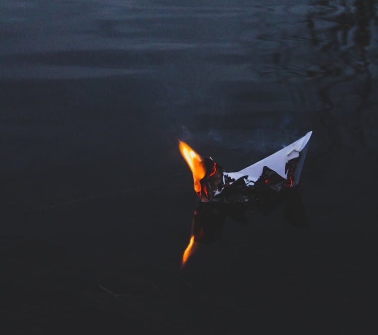Origami Paper Boat Floating On Water And Burning In Dark