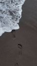 From above of foamy waves of sea washing sandy beach with footprints on summer day