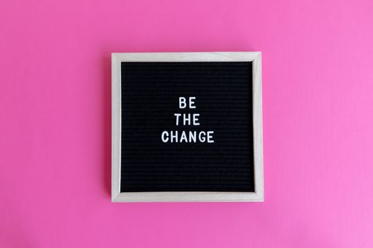 Letterboard with 'Be the Change' on a vibrant pink background.