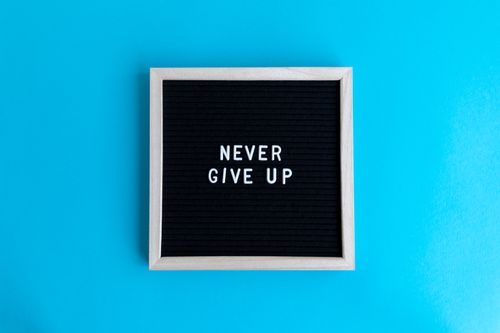 Free Black letter board with 'Never Give Up' message on a vibrant blue background. Stock Photo