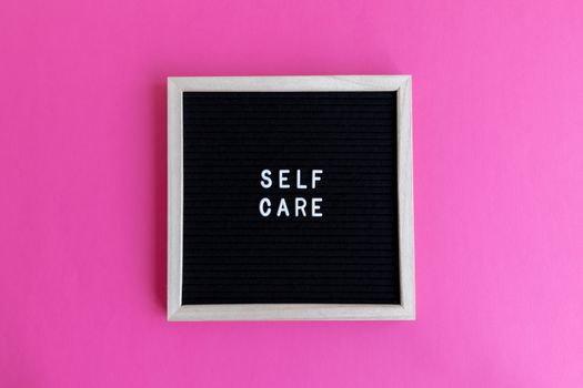 A motivation message 'Self Care' displayed on a letter board against a pink backdrop.