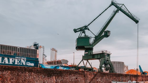Aerial view of a large green crane at an industrial port under a cloudy sky.
