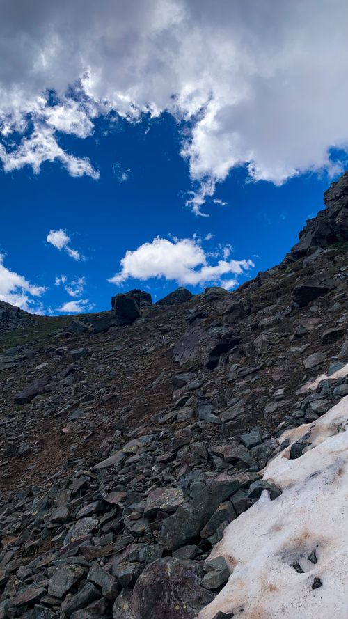 Free Capture of a rugged rocky mountainside under a vibrant blue sky with scattered clouds. Stock Photo