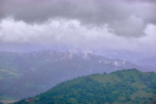 A tranquil mountain range shrouded in mist and clouds, showcasing lush greenery in spring.
