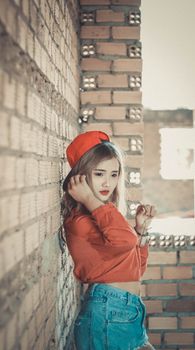 一位穿着时尚的年轻女子身着休闲装，靠在砖墙上摆姿势