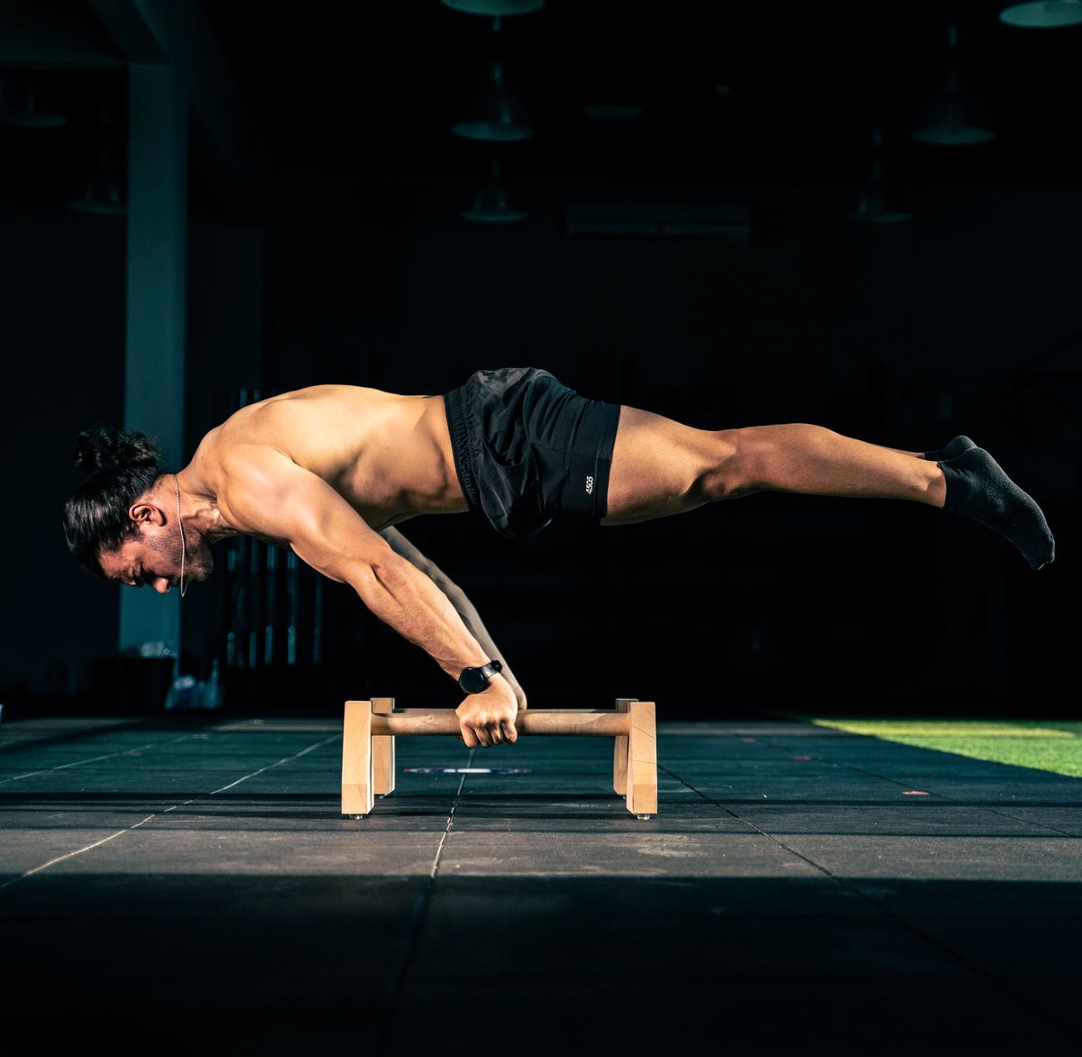 Homme torse nu tenant une planche complète sur des parallettes en bois, corps parfaitement horizontal au-dessus du sol