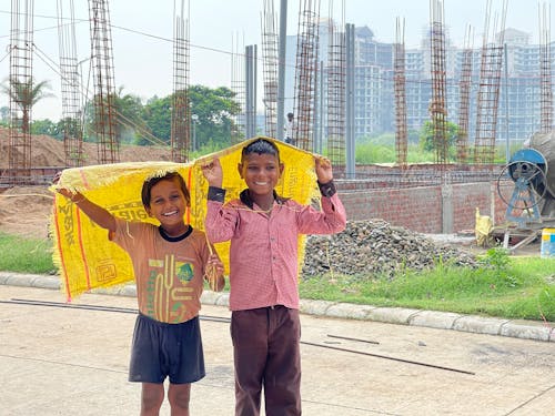 Two Young Boys Smiling while Holding a Yellow Sack Near at the Construction Site