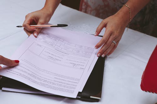 Person Holding Pen and White Printer Paper