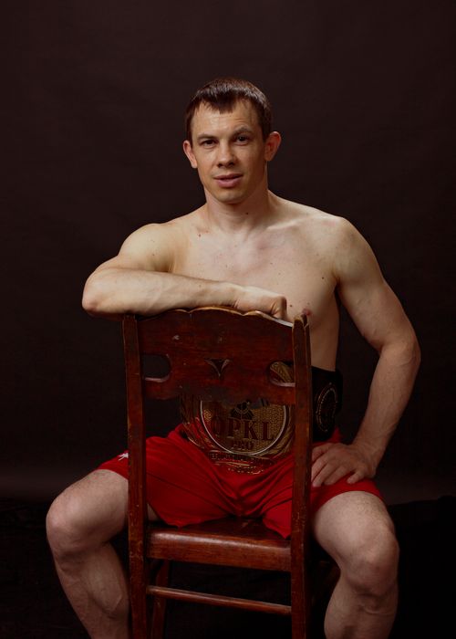 Free A shirtless man poses with a championship belt behind a wooden chair against a dark background. Stock Photo