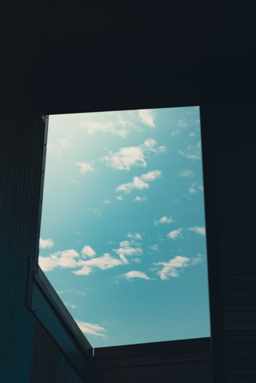 Free A view of blue sky and white clouds framed by building walls. Stock Photo