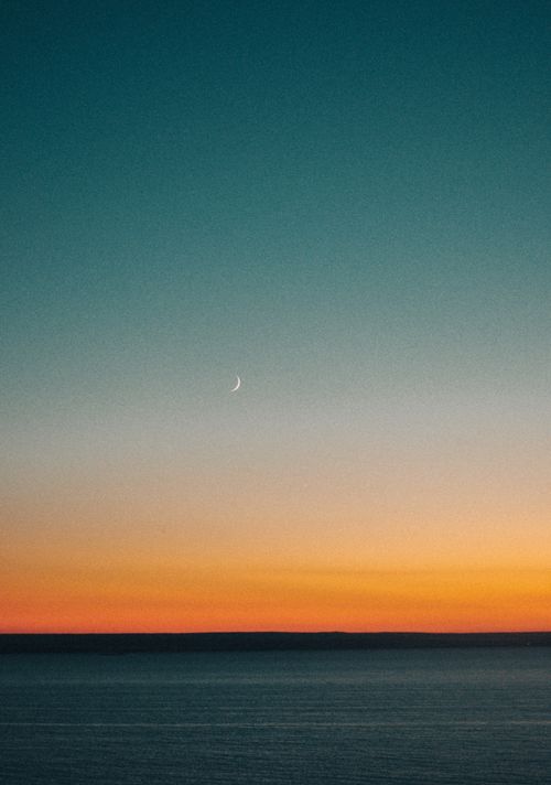 Free A tranquil ocean scene captures a crescent moon and vibrant sunset sky, creating stunning natural beauty. Stock Photo