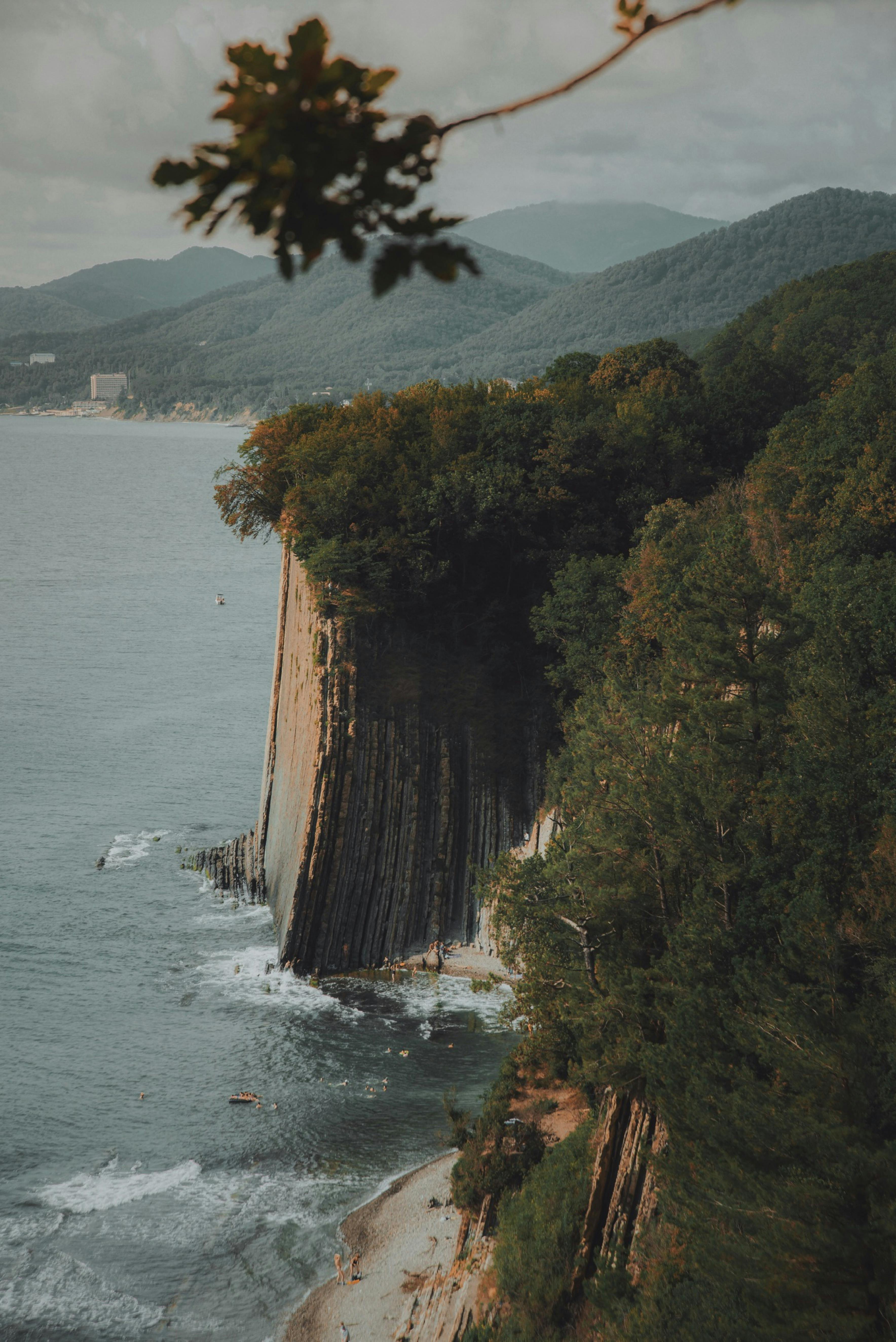 Dramatic cliffside view overlooking the ocean with lush trees and mountains.