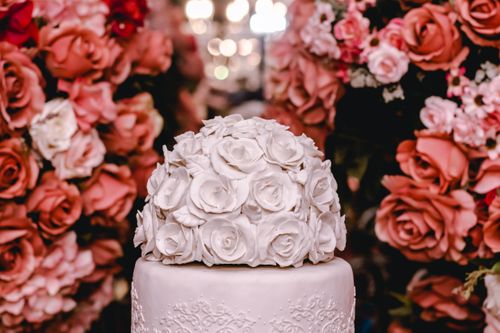 Free A beautifully decorated white rose cake surrounded by vibrant floral arrangements, perfect for weddings. Stock Photo