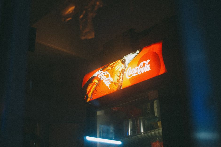 A Coca-Cola cooler illuminated in low light with a vintage aesthetic, displaying iconic branding.