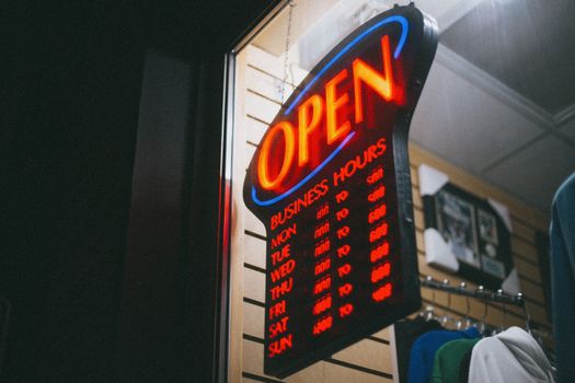 Vibrant neon 'Open' sign displaying business hours inside a shop at night.