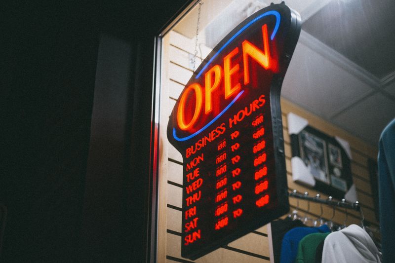 Vibrant neon 'Open' sign displaying business hours inside a shop at night.