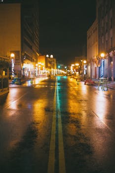 A deserted city street at night, reflecting warm lights on wet pavement.
