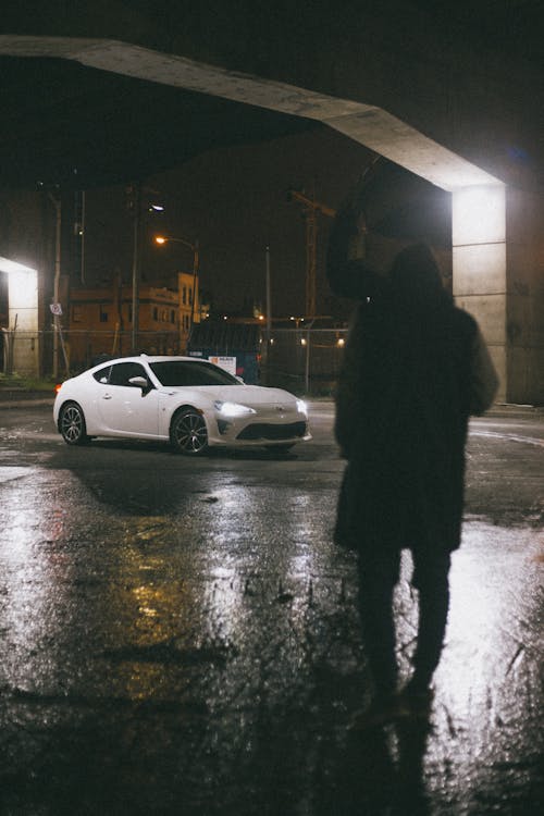 Silhouette of a Person Walking Near a White Car